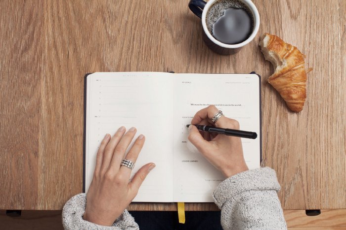 Woman making notes on a table with coffee and a croissant